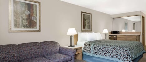 Una habitación de hotel con sofá, cama con ropa de cama estampada, mesita de noche con lámparas y un espejo grande en la pared.