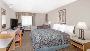 Une chambre d’hôtel avec un lit, un bureau équipé d’un ordinateur, une chaise, une télévision et une lampe.