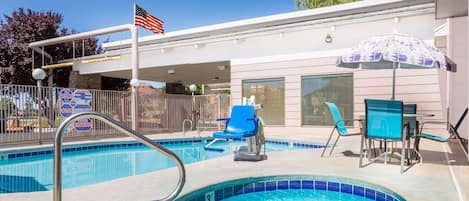 A pool area with a hot tub, lounge chairs, and a flag.
