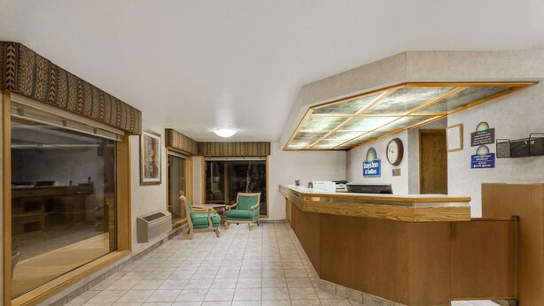 Un espace d’accueil avec un comptoir de réception en bois, deux chaises vertes, une grande fenêtre et une horloge au mur.