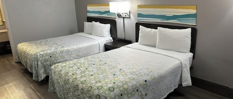 A hotel room with two beds, each with a patterned bedspread, a nightstand with a lamp, and a painting on the wall.