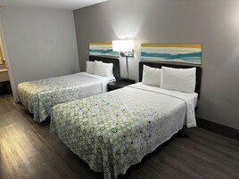 Habitación de hotel con dos camas, cada una con una colcha estampada, una mesita de noche con lámpara y un cuadro en la pared.