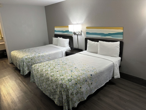 A hotel room with two beds, each with a patterned bedspread, a nightstand with a lamp, and a painting on the wall.