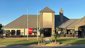 A hotel with a modern design, featuring a prominent entrance, a flagpole, and a landscaped front yard with palm trees. - HomeTowne Studios by Red Roof Birmingham - Highway 280 (Birmingham)