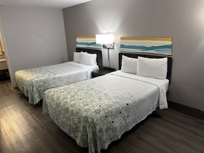 Quarto de hotel com duas camas, cada uma com colcha estampada, uma mesa de cabeceira com abajur e um quadro na parede.