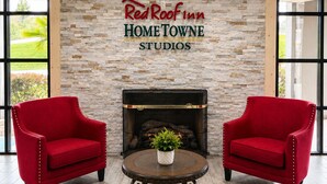 A Red Roof Inn HOME TOWNE STUDIOS lobby with a stone wall, two red armchairs, a fireplace, and a round table with a plant. - HomeTowne Studios by Red Roof Birmingham - Highway 280 (Birmingham)
