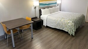 A hotel room with a bed, a desk, two chairs, a nightstand, and a painting on the wall. - HomeTowne Studios by Red Roof Birmingham - Highway 280 (Birmingham)