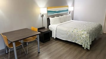 A hotel room with a bed, a desk, two chairs, a nightstand, and a painting on the wall.