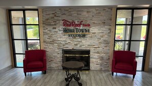 A Red Roof Inn HOME TOWNE STUDIOS room with a fireplace, two red armchairs, and large windows. - HomeTowne Studios by Red Roof Birmingham - Highway 280 (Birmingham)