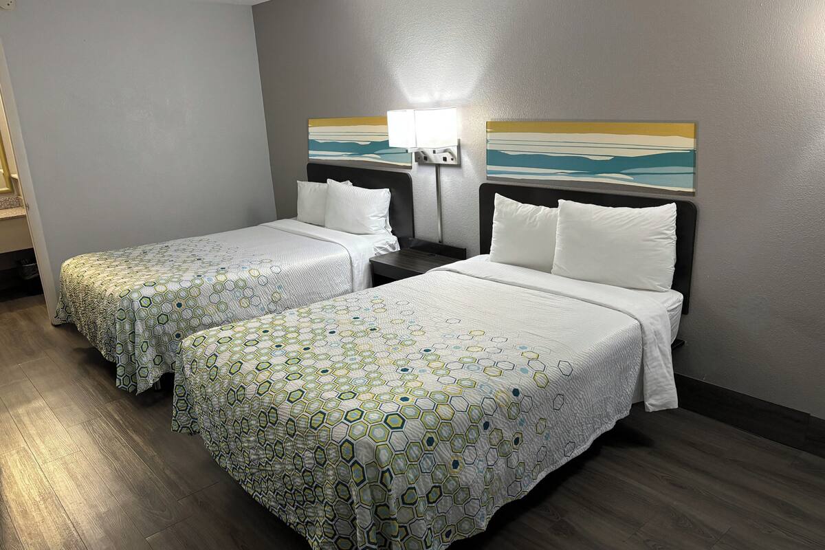 A hotel room with two beds, each with a patterned bedspread, a nightstand with a lamp, and a painting on the wall.