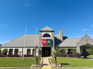 A hotel with a red and green sign, a peaked roof, and a flagpole. - HomeTowne Studios by Red Roof Birmingham (Birmingham)