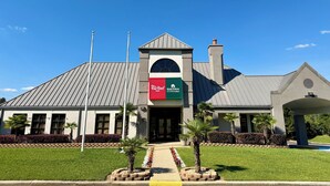 A hotel with a red and green sign, a peaked roof, and a flagpole. - HomeTowne Studios by Red Roof Birmingham - Highway 280 (Birmingham)
