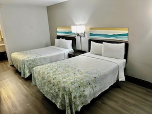 Quarto de hotel com duas camas, uma mesa de cabeceira, uma luminária e um quadro na parede.