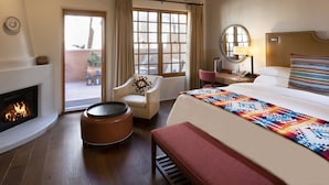 Habitación de hotel con techo de madera, chimenea, cama con manta de colores, escritorio con lámpara y una silla.