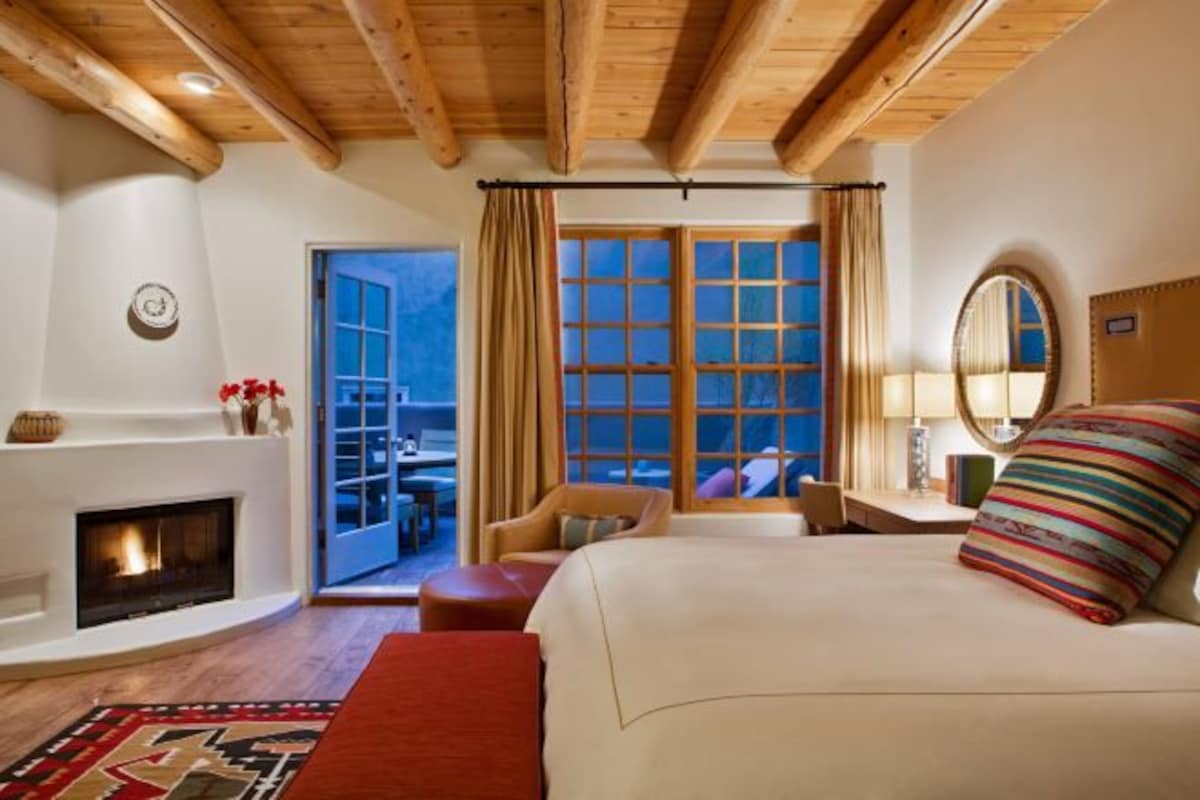A bedroom with a fireplace, a large bed, a window with curtains, and a view of the outside.