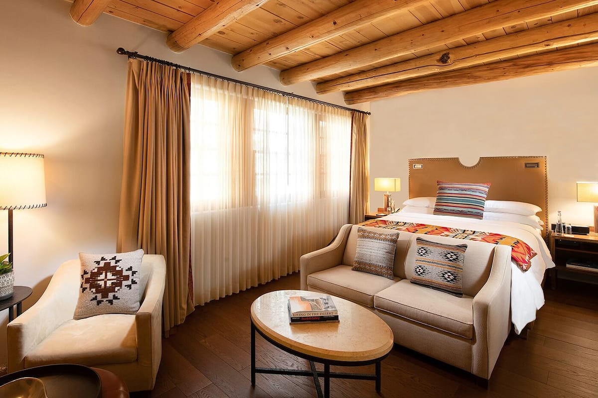 Una habitación de hotel con techo de madera, una cama con cabecero, un sofá, una mesa de centro y una silla.