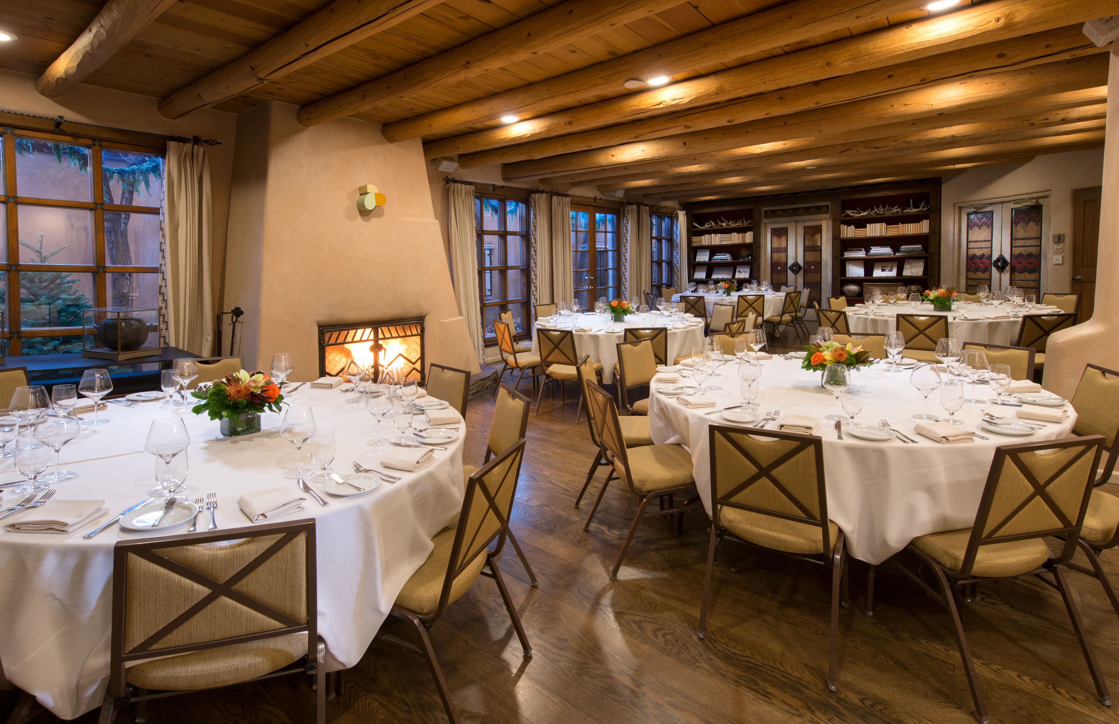 Un restaurante con mesas redondas preparadas para comer, pisos de madera y un ambiente cálido.