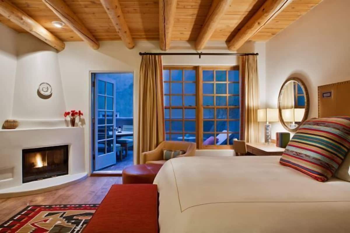 Un dormitorio con chimenea, una cama grande, una ventana con cortinas y vistas al exterior.