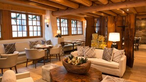 Un interior acogedor y bien iluminado con vigas de madera, asientos cómodos y grandes ventanales con vistas a palmeras.