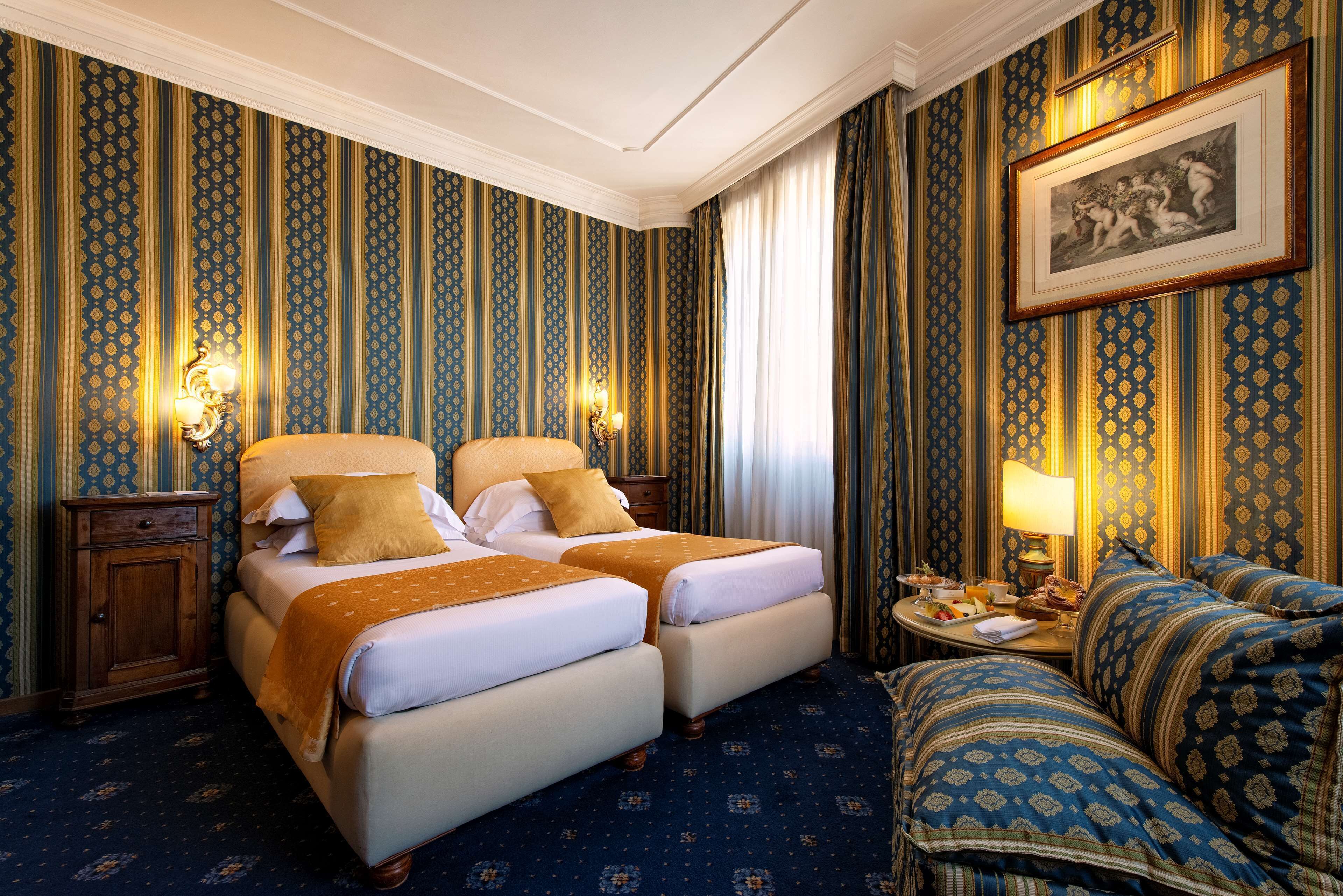 Une chambre d’hôtel avec deux lits, un canapé, une table de chevet et un tableau encadré au mur.
