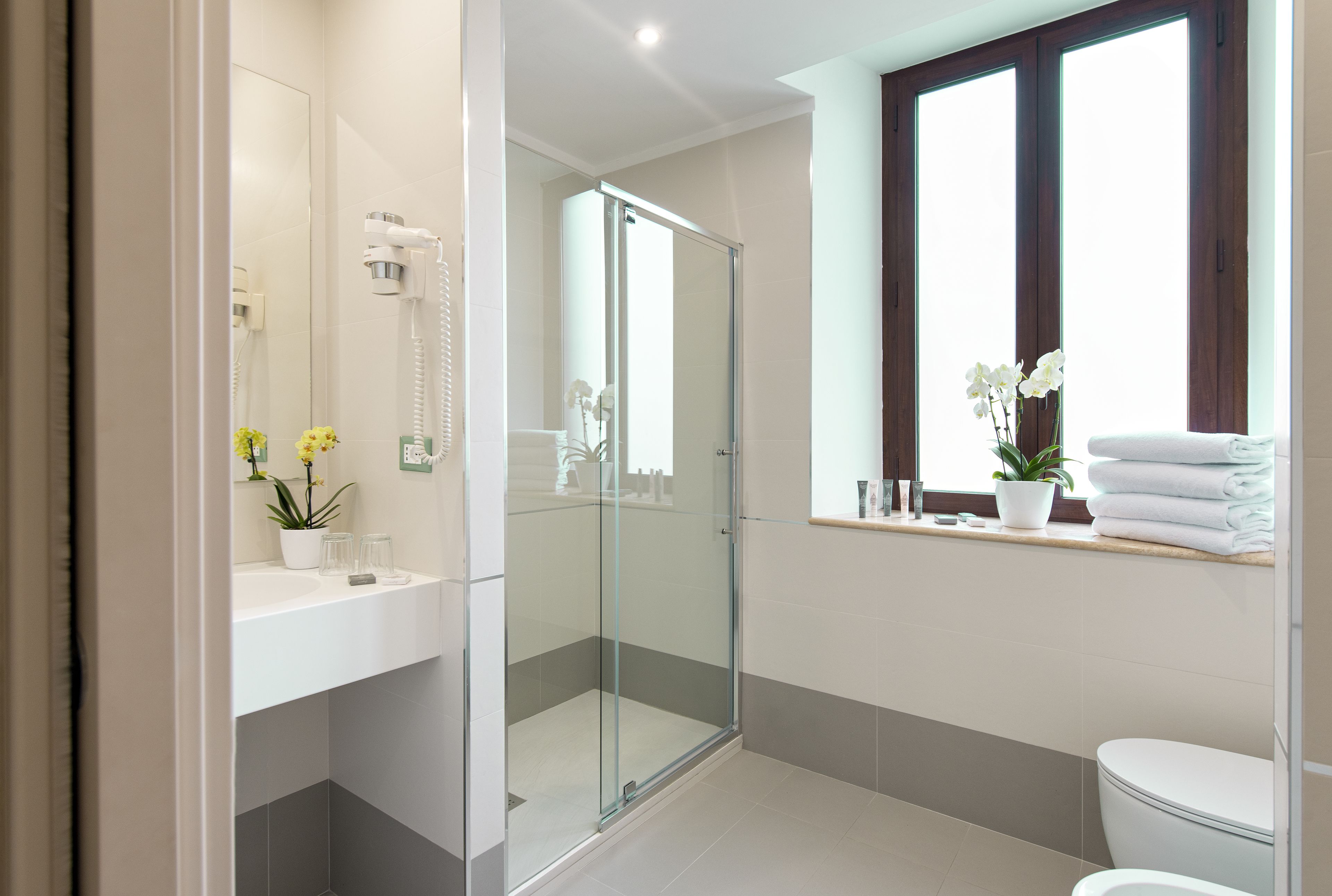 A modern bathroom with a glass-enclosed shower, a white sink with a mirror, and a window with a view.