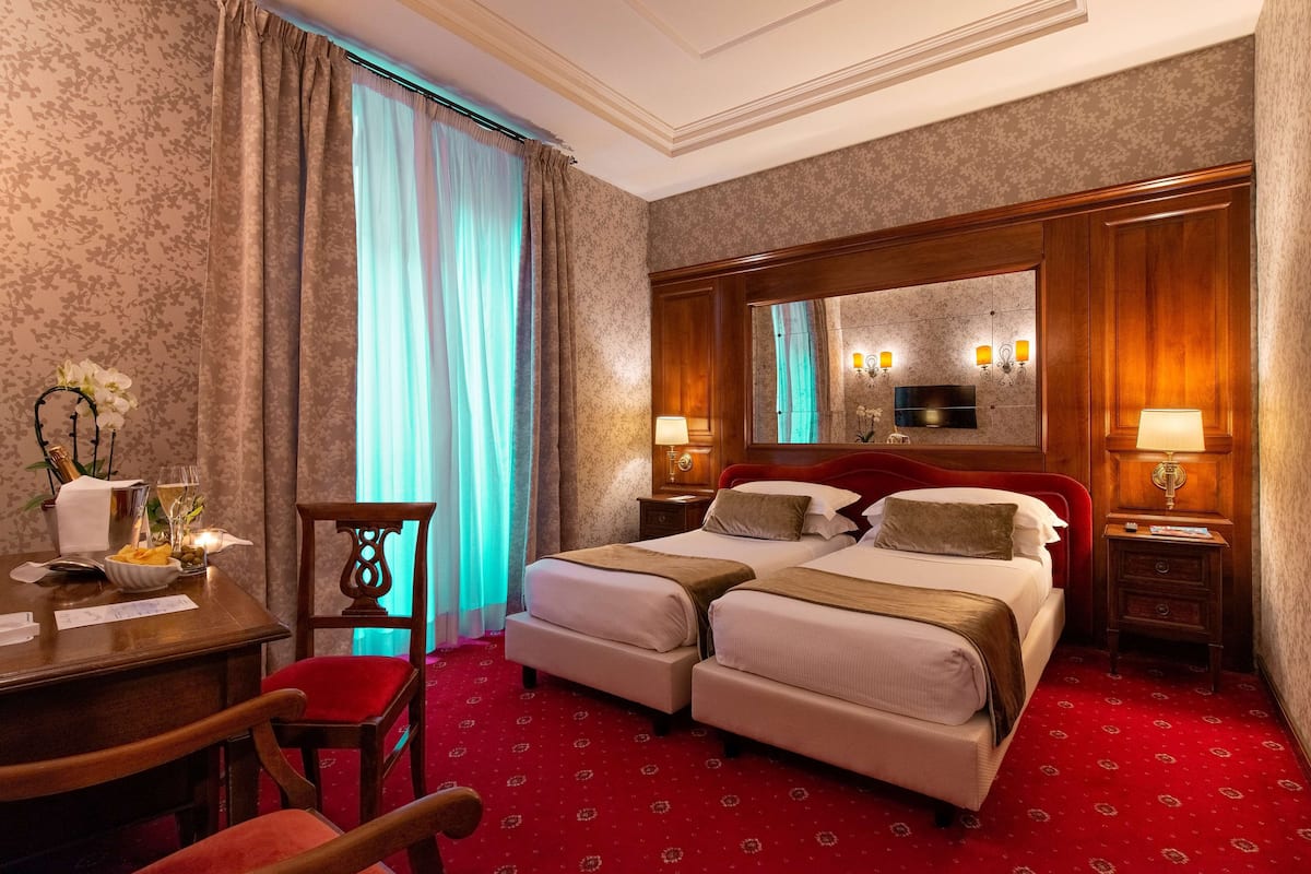 A hotel room with two beds, a desk, a chair, and a mirror.