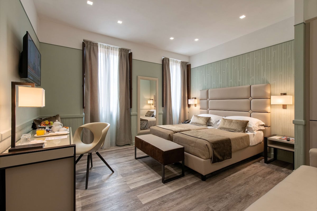 A modern hotel room with a large bed, bedside tables, a desk with a chair, and a television.