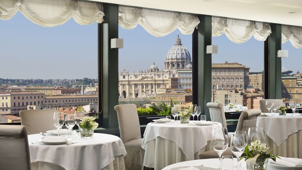 Un restaurant dont les tables sont dressées pour le service, offrant une vue sur un bâtiment historique.
