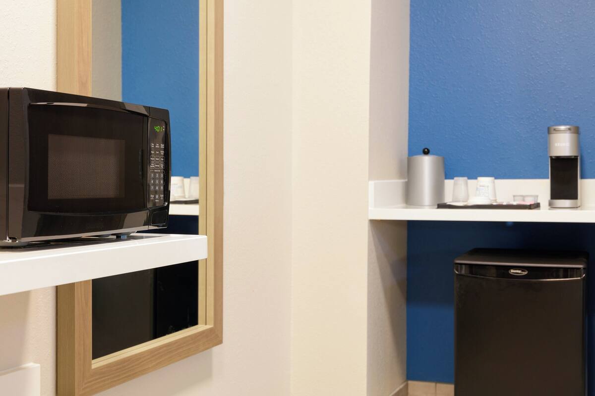 A microwave on a white shelf, a coffee maker, and a trash bin in a kitchen area.