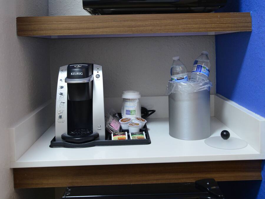 A kitchenette with a microwave, coffee maker, and water bottles on a white countertop.
