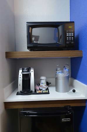 A kitchenette with a microwave, coffee maker, and water bottles on a white countertop.