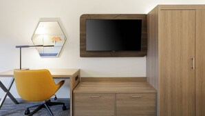 Et moderne værelse med skrivebord, gul stol, ophængt TV og et træskab.