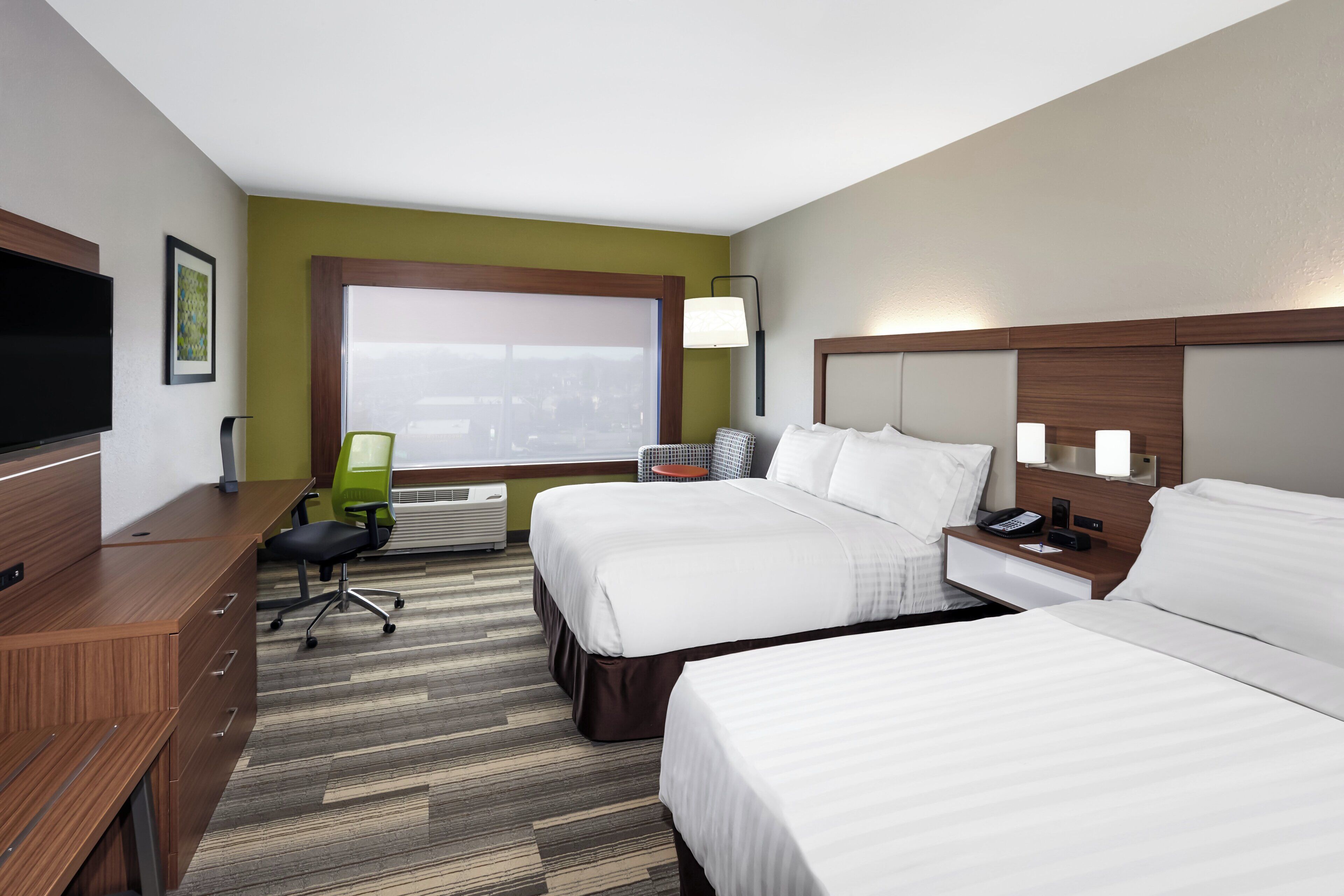 A hotel room with two beds, a desk, a chair, a TV, and a window with blinds.