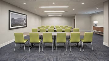 Une salle de conférence avec une grande table et des chaises vertes, un sol recouvert de moquette et un tableau représentant un paysage urbain encadré au mur.