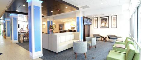 A modern lobby with a reception desk, seating area, and a large window.