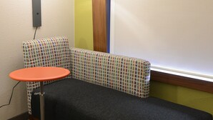 Et hjørneværelse med sofa, lille bord og væglampe.
