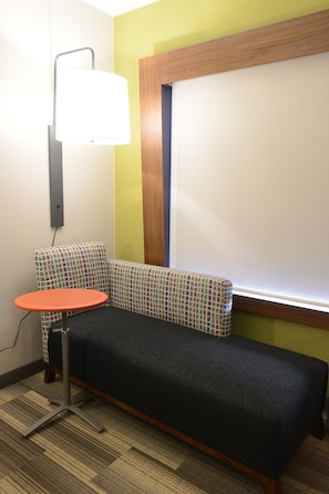 Une pièce d’angle avec un canapé, une petite table et une lampe fixée au mur.
