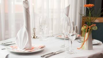 A table set for a formal dining experience with white tablecloths, clear glassware, and a vase with a flower arrangement.