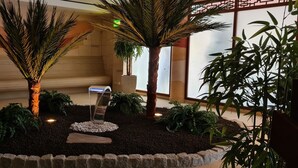 Un jardin intérieur circulaire agrémenté de palmiers et de fougères, d’un élément décoratif aquatique et d’un sentier en pierre.