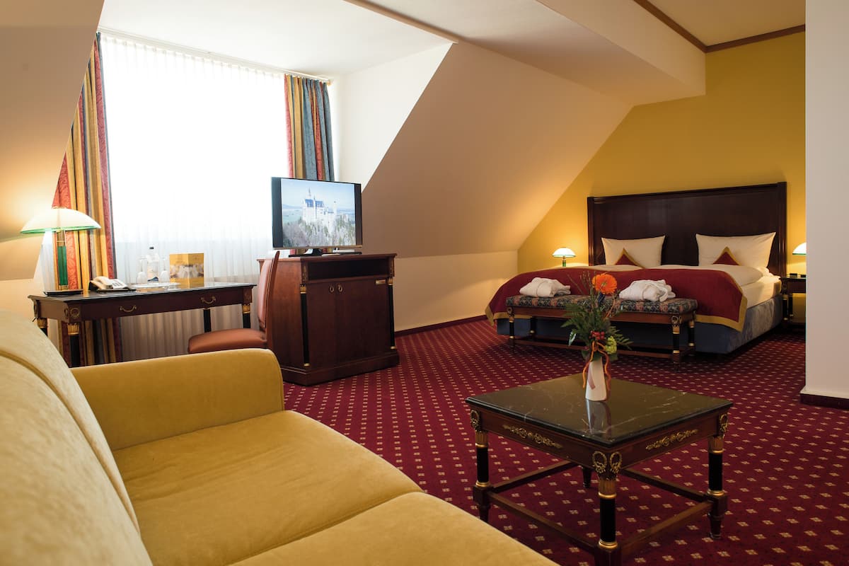 Quarto de hotel com cama, escrivaninha, televisão, sofá e mesa de centro.