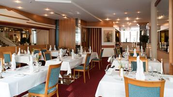 A restaurant with multiple tables set for dining, featuring white tablecloths, blue upholstered chairs, and candles.