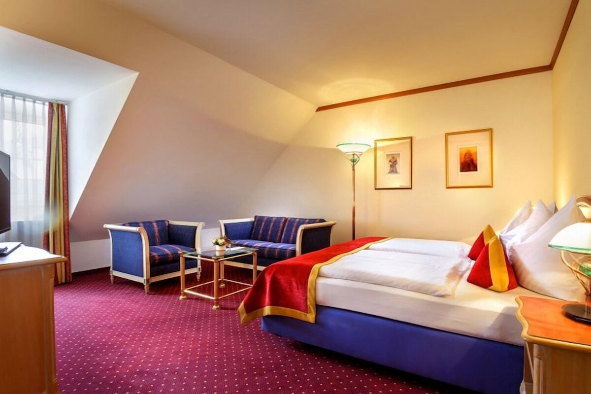 Una habitación de hotel con una cama, dos sillones, un escritorio, una lámpara y un televisor.