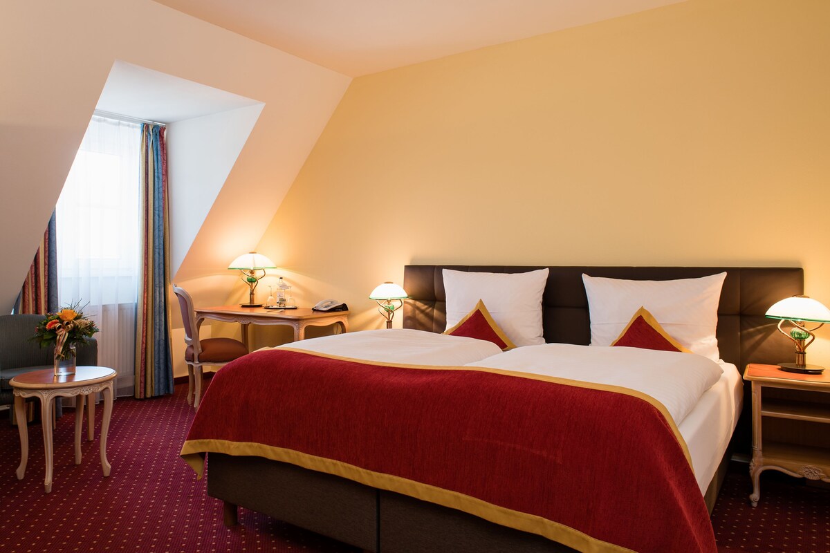 Una habitación de hotel con una cama, un escritorio, una silla y una mesita de noche con una lámpara.