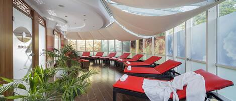 A spa area with red lounge chairs, a large potted plant, and a view through the windows.