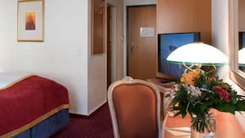 Una habitación de hotel con una cama, un escritorio con lámpara, una silla, un televisor y una puerta.