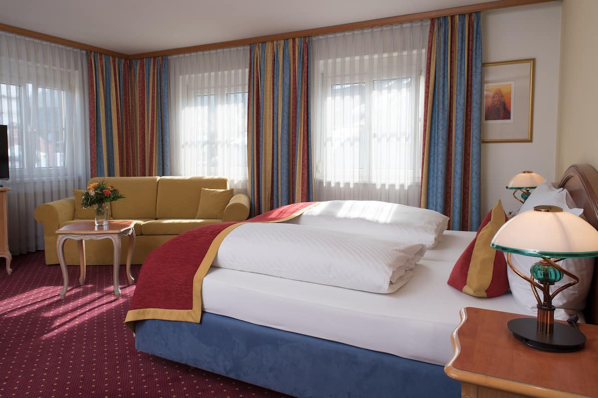 Quarto de hotel com cama, sofá, televisão e cortinas.