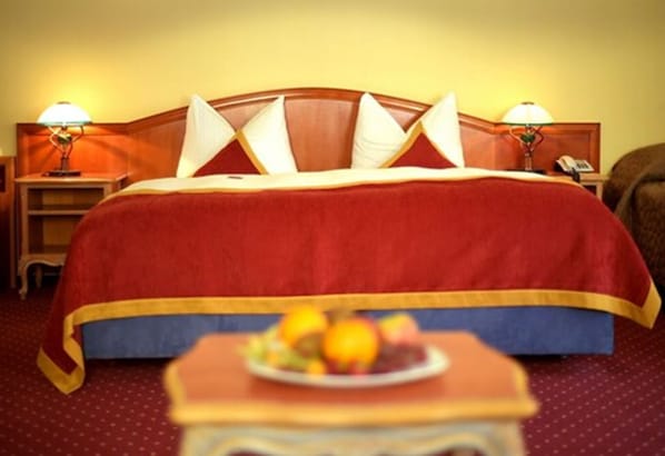 Habitación de hotel con una cama grande, dos mesitas de noche con lámparas y una cesta de fruta sobre una mesita auxiliar.