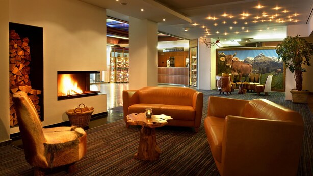 Un hall d’entrée moderne avec des canapés en cuir, une cheminée, un comptoir d’accueil et une grande fenêtre donnant sur les montagnes.
