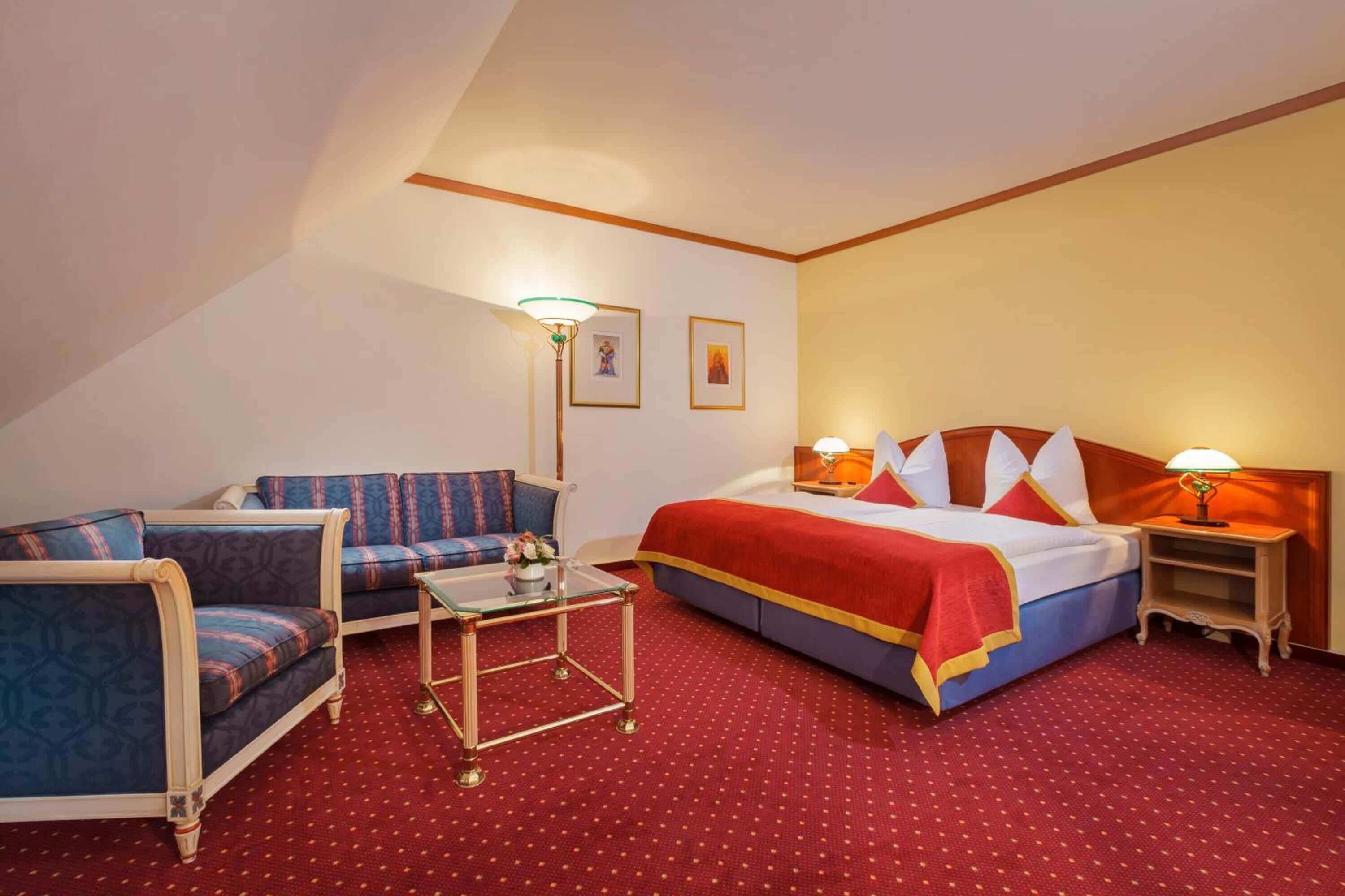 A hotel room with a bed, a sofa, a small table, and a nightstand.