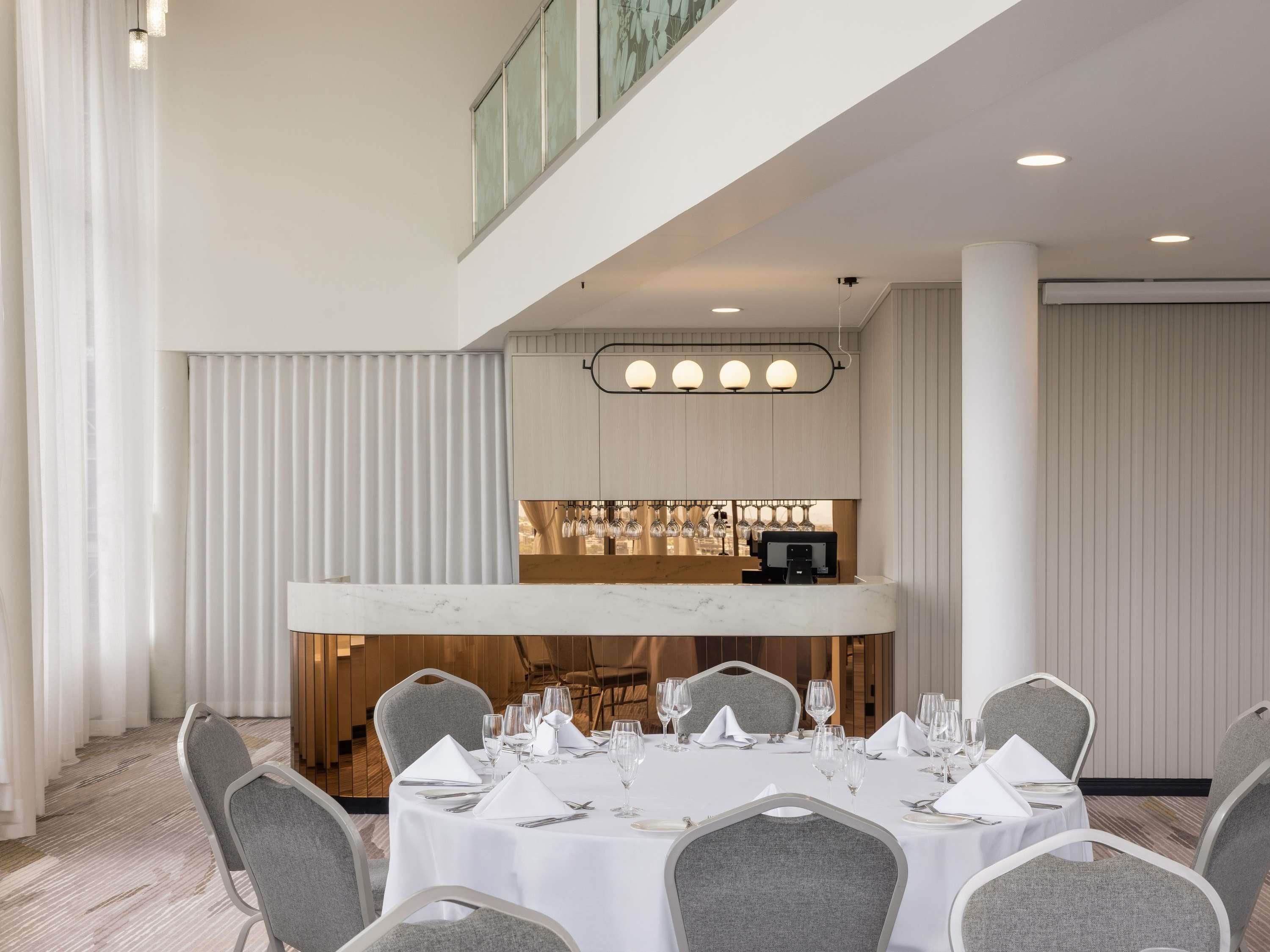 A dining area with a marble bar, grey upholstered chairs, and a white tablecloth-covered table.